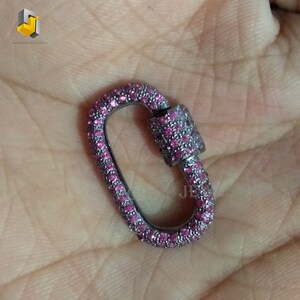 Puede incluir: Un cierre ovalado plateado con un diseño de piedras rosas. El cierre está cubierto de pequeñas piedras rosas.