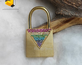 May include: Gold padlock with a rainbow-colored triangle design made of small gemstones. The padlock is on a white surface with a piece of wood behind it.