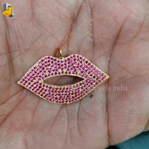 May include: Gold-tone pendant shaped like a pair of lips, encrusted with pink cubic zirconia stones.
