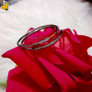 Puede incluir: Un par de pendientes de aro de plata con una fila de peque&ntilde;os diamantes alrededor del borde. Los pendientes est&aacute;n sobre un fondo rojo.