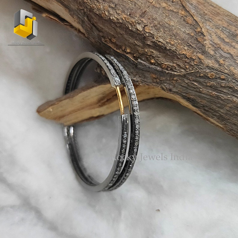 Puede incluir: Un par de pendientes de aro de plata con una fila de peque&ntilde;os diamantes alrededor del borde. Los pendientes est&aacute;n sobre una superficie de madera.