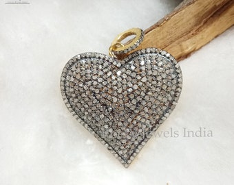 May include: A silver heart-shaped pendant with a gold bail, covered in small diamonds. The pendant is on a white surface.