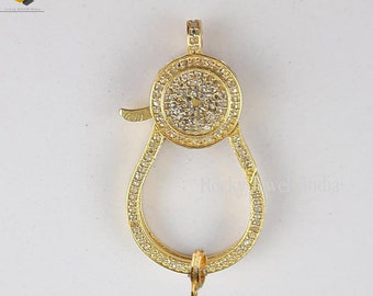 May include: Gold-tone clasp with a round, pave-set center and a pear-shaped loop. The clasp is adorned with clear cubic zirconia stones.