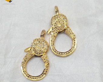May include: Two gold-toned clasps with clear stones set in the metal. The clasps are oval-shaped and have a small loop at the top.