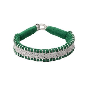 May include: A green and silver bracelet. The bracelet features a woven green band with a silver clasp. The center of the bracelet has a row of silver links with embedded clear stones. The bracelet is a fashion accessory.