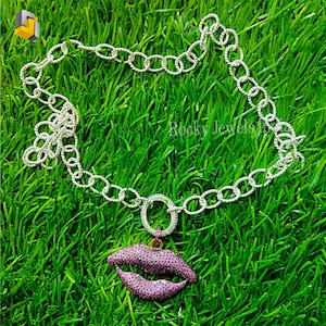 May include: A silver chain necklace with a pink lip charm. The chain is made of small, linked circles. The lip charm is set with pink stones.