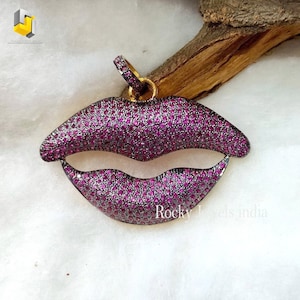 May include: A gold and black pendant shaped like a pair of lips, encrusted with small pink gemstones.