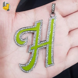 May include: A pendant in the shape of the letter "H" with a lime green enamel finish. The pendant is outlined with small, sparkling stones and has a silver-colored bail.