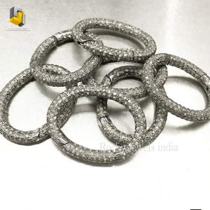 May include: A set of five silver diamond bracelets, each with a round shape and a textured surface. The bracelets are arranged in a pile, with some overlapping.