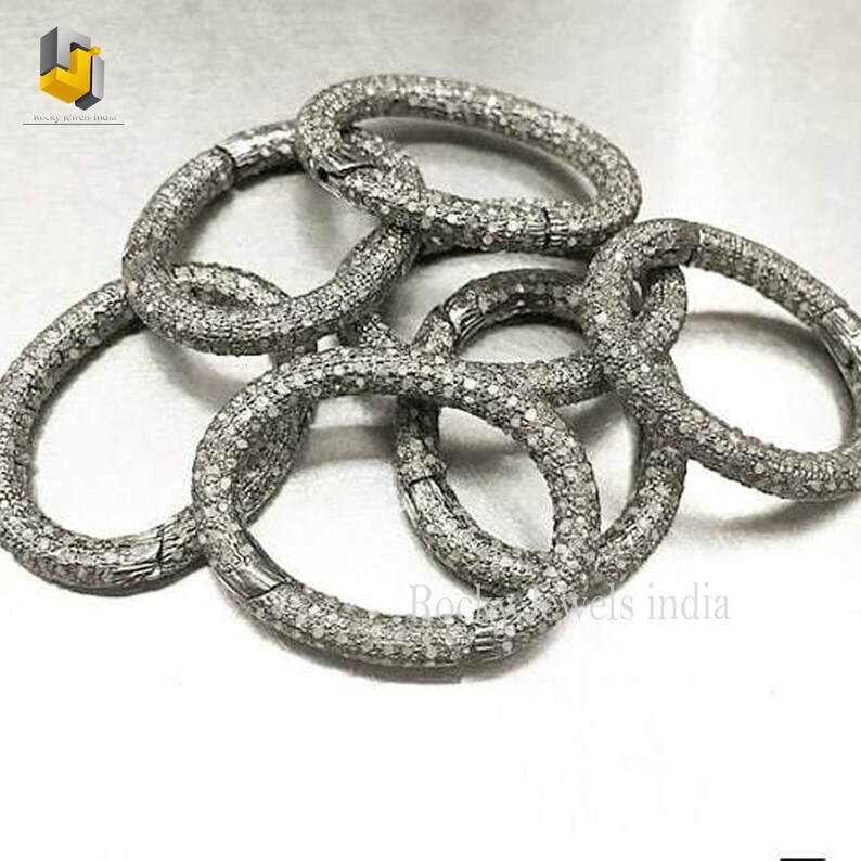 May include: A set of five silver diamond bracelets, each with a round shape and a textured surface. The bracelets are arranged in a pile, with some overlapping.