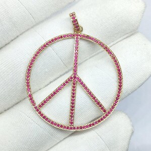 May include: A gold peace sign pendant with pink gemstones. The pendant is made of 14k gold and is set with round pink gemstones.