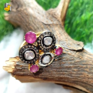 May include: A gold ring with three round settings, each containing a white diamond surrounded by smaller black diamonds. The ring also features four pink gemstones.