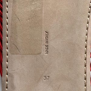 May include: The beige suede sole of a shoe features the embossed text MADE IN ITALY and the number 37. A red corded detail is visible along the left edge, and light-colored stitching runs along the perimeter of the sole.