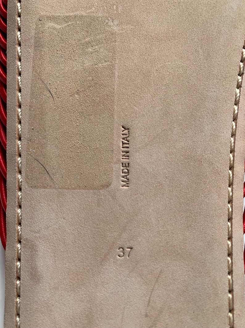 May include: The beige suede sole of a shoe features the embossed text MADE IN ITALY and the number 37. A red corded detail is visible along the left edge, and light-colored stitching runs along the perimeter of the sole.