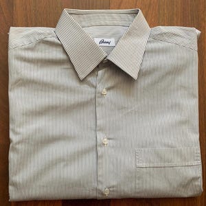May include: Folded button-down shirt with a striped pattern in shades of white and brown. The shirt features a classic collar, a chest pocket, and the brand name "Brioni" on the collar.