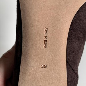 May include: The sole of a dark brown shoe featuring a smooth beige centre panel. The text MADE IN ITALY is embossed vertically in the centre, with the number 39 printed below it. The shoe has a dark brown suede-like texture on the sides.