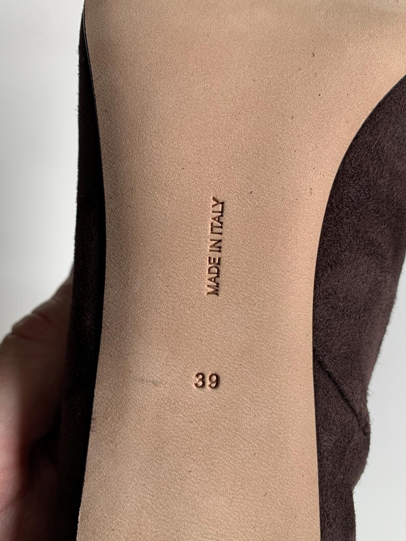 May include: The sole of a dark brown shoe featuring a smooth beige centre panel. The text MADE IN ITALY is embossed vertically in the centre, with the number 39 printed below it. The shoe has a dark brown suede-like texture on the sides.