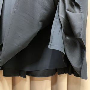 K&ouml;nnte beinhalten: Nahaufnahme eines dunkelblauen Rocks mit einem mehrschichtigen Design. Der Rock hat eine plissierte Au&szlig;enschicht und ein glattes, dunkleres Innenfutter. Der Stoff scheint ein weiches, flie&szlig;endes Material zu sein.