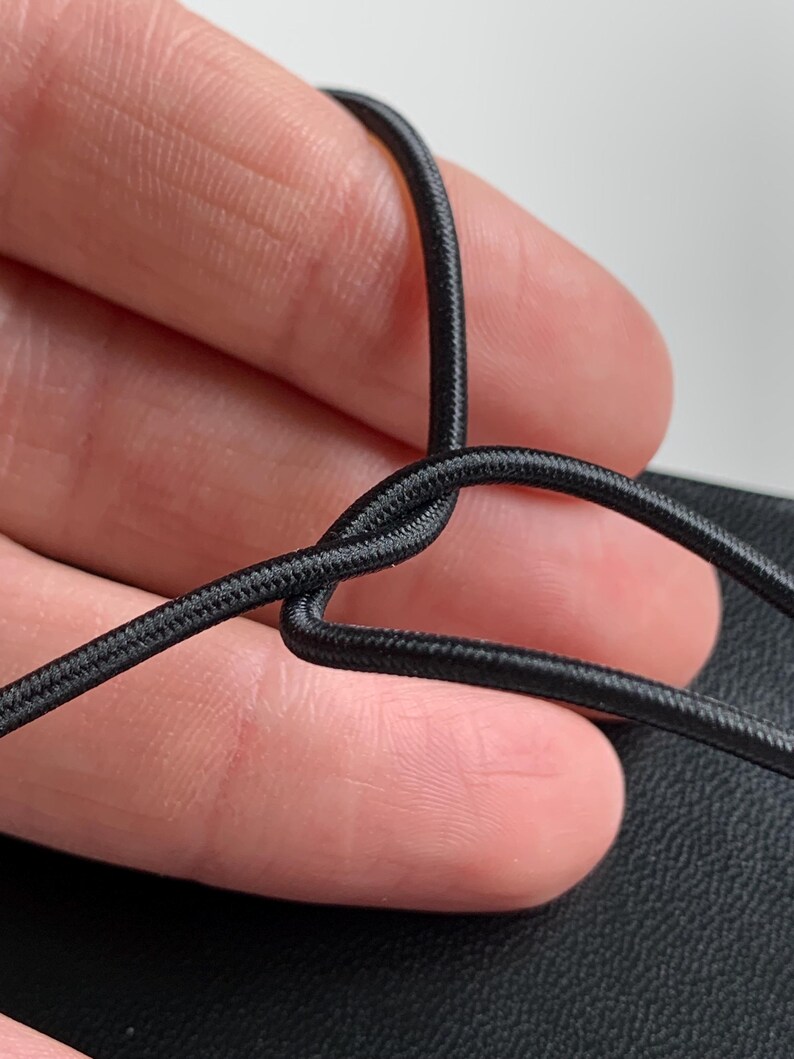 May include: A thin, black, flexible elastic cord with a woven, textured surface. The cord is bent into a loop shape, showing its round profile and consistent dark black colour throughout the entire length of the material visible in the frame.