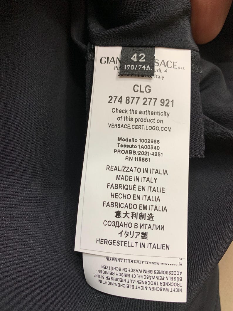 K&ouml;nnte beinhalten: Ein schwarzes Kleidungsst&uuml;cketikett mit wei&szlig;em Text, einschlie&szlig;lich des Markennamens, der Gr&ouml;&szlig;e 42 und eines Produktcodes. Das Etikett enth&auml;lt auch den Text "Made in Italy" und Pflegehinweise.