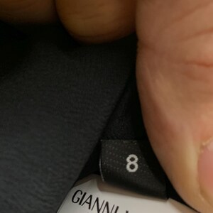 K&ouml;nnte beinhalten: Schwarzes Etikett mit der wei&szlig;en Zahl 8. Darunter ein wei&szlig;es Etikett mit dem Text "GIANNI VERSACE" und der Adresse "Piazza Luigi Einaudi 20124 Mila".
