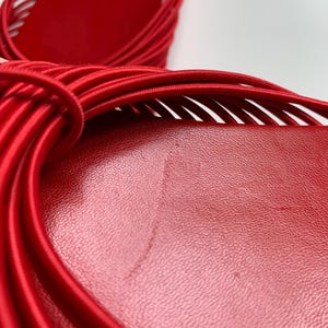 May include: A pair of bright red sandals featuring a smooth, textured footbed and a series of thin, elasticized cord straps that wrap across the top. The design showcases a vibrant monochromatic red color scheme with a focus on the intricate cord detailing.