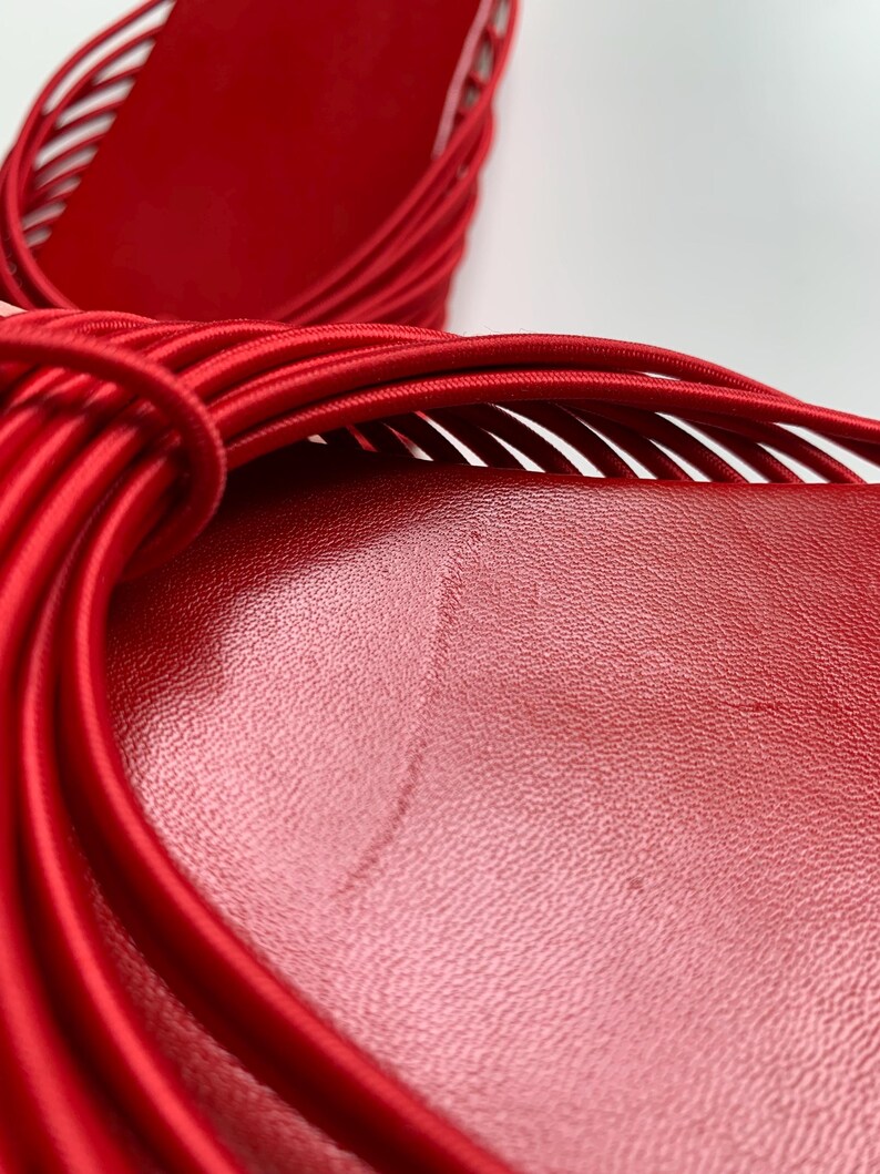 May include: A pair of bright red sandals featuring a smooth, textured footbed and a series of thin, elasticized cord straps that wrap across the top. The design showcases a vibrant monochromatic red color scheme with a focus on the intricate cord detailing.