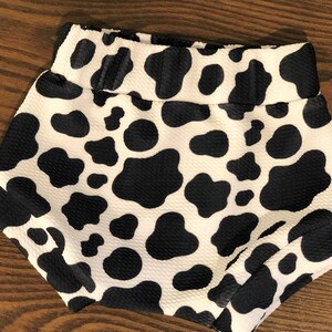 May include: Black and white cow print baby shorts. The shorts are made of a soft, stretchy fabric and have an elastic waistband.