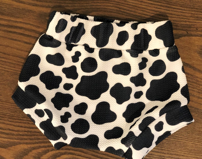May include: Black and white cow print baby shorts. The shorts are made of a soft, stretchy fabric and have an elastic waistband.