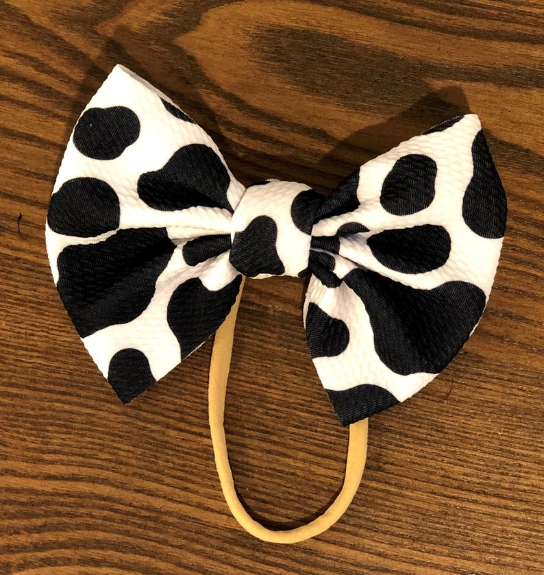 May include: A black and white cow print hair bow with a nude elastic headband.