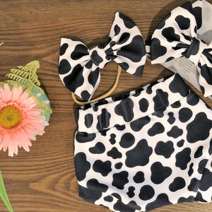 May include: A black and white cow print headband, a matching diaper cover, and a larger headband with a bow.