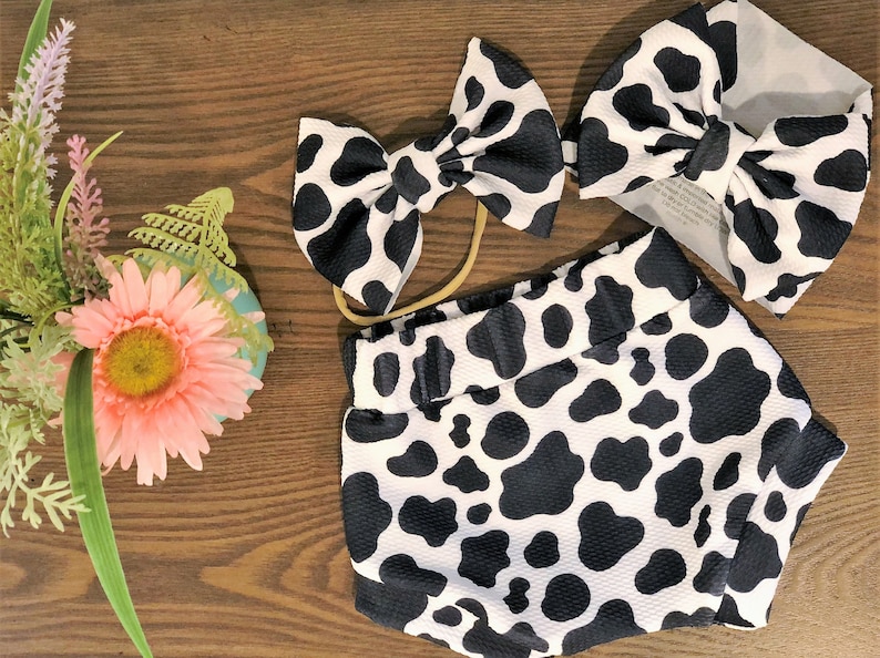 May include: A black and white cow print headband, a matching diaper cover, and a larger headband with a bow.