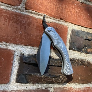 May include: A silver pocket knife with a textured handle and a partially open blade. The knife is attached to a brick wall.