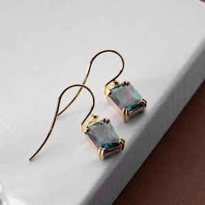 May include: A pair of gold-colored drop earrings with rectangular, iridescent gemstones. The earrings have a simple, elegant design, with a hook closure. The gemstones display a range of colors, including blues, greens, and purples.