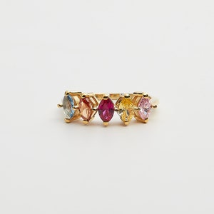 May include: A gold ring with a row of colorful marquise-shaped gemstones. The stones are blue, pink, red, yellow, and light pink.