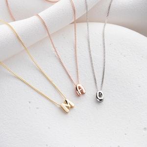 Könnte beinhalten: Drei Initialen-Halsketten in Gold, Roségold und Silber. Die goldene Halskette zeigt den Buchstaben "M", die roségoldene Halskette den Buchstaben "A" und die silberne Halskette den Buchstaben "O". Jede Halskette hat eine zarte Kette.