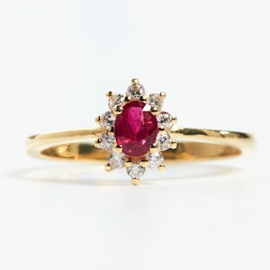 May include: A gold ring with a red oval gemstone surrounded by smaller white gemstones.