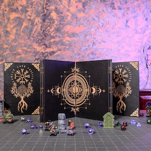 May include: A black, three-panel tabletop game screen with gold geometric designs and runes. The screen is open, revealing a game setup with miniature figures, dice, and terrain pieces. The background is a textured wall.