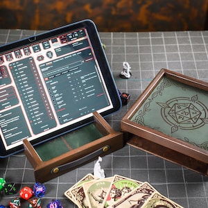 Pode incluir: Uma caixa de jogo em madeira escura com tampa verde apresentando um gráfico de dado de 20 faces, uma gaveta de madeira a condizer com puxador em pele, um tablet com ficha de personagem digital, vários dados poliédricos coloridos e cartas.