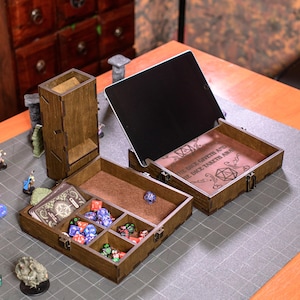 May include: Wooden dice rolling and storage set with a dice tower, two storage boxes, and an open tablet. The boxes are divided into compartments and contain dice and cards. The set is brown with a dark interior and is designed for tabletop gaming.