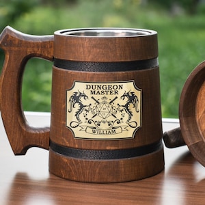 May include: A dark brown wooden mug with a metal interior and a handle. A gold-coloured plaque on the front features the text "DUNGEON MASTER" above a 20-sided die graphic flanked by two dragons, with the name "WILLIAM" printed at the bottom.