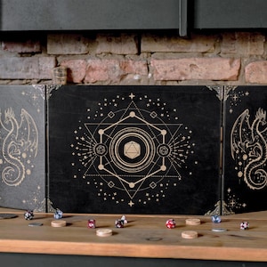 Puede incluir: Tablero de juego de mesa de madera negra con un diseño geométrico que presenta un dragón y una estrella de cinco puntas. El tablero está dividido en tres secciones, cada una con un diseño diferente. El tablero está rodeado de dados y otras piezas de juego.