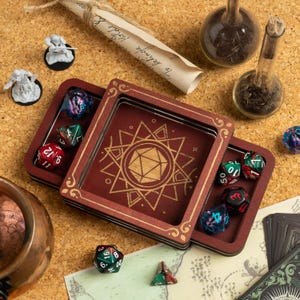 Könnte beinhalten: Ein burgunderfarbener Würfelbehälter aus Holz mit goldenen Akzenten und einem geometrischen Muster. Der offene Behälter enthält mehrere vielseitige Würfel in verschiedenen Farben. Weitere Artikel sind Miniaturfiguren, Schriftrollen und Glasfläschchen.