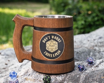 May include: A brown wooden tankard with a stainless steel interior, featuring a black circular emblem with a gold 20-sided die graphic and the text "DON'T WORRY I HAVE A PLAN" and "FUCK" printed on the die face, accented by two black bands.