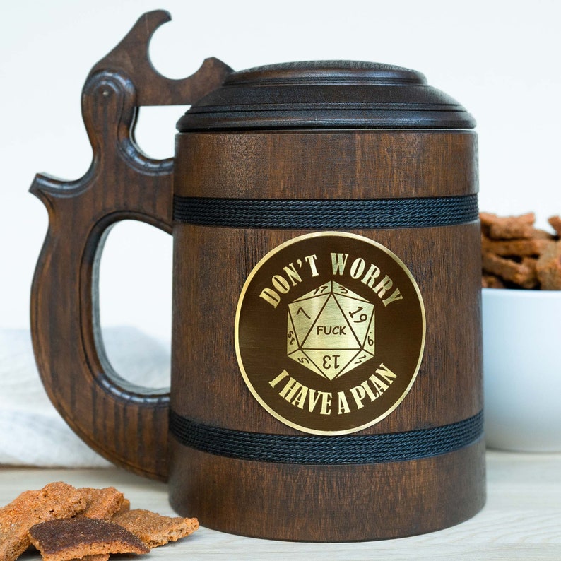 May include: A dark brown wooden beer stein with a lid and a unique handle. The stein has a gold emblem with the text "DON'T WORRY, I HAVE A PLAN" and a D20 die graphic. Black rope accents the design.