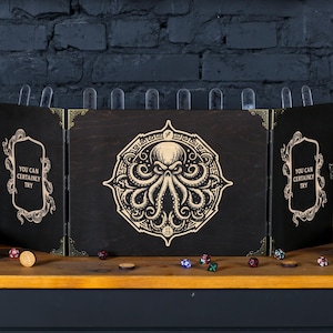 Puede incluir: Una torre de dados de madera negra con un diseño de Cthulhu. La torre tiene tres paneles, cada uno con un diseño diferente. El panel central presenta un Cthulhu con tentáculos. Los paneles laterales tienen el texto "Puedes intentarlo ciertamente".