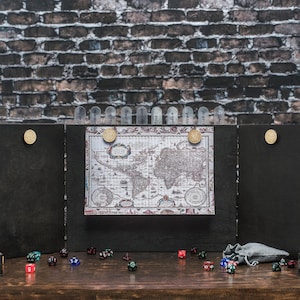 Op de afbeelding: Een houten tabletop-gameset met een wereldkaartdisplay, dobbelstenen en dobbelsteentorens. De set bevat een vouwscherm, dobbelstenen en een kleine zak. De achtergrond is een bakstenen muur.