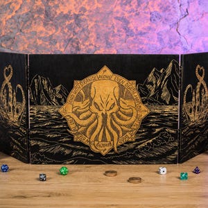 May include: A four-panel black wooden dungeon master screen featuring gold-coloured laser-engraved artwork of a tentacled creature, mountains, and waves. The central panel displays the text: And with strange aeons even death may die.