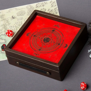 Pu&ograve; includere: Un vassoio per dadi in legno con interno rosso e design geometrico nero. Il vassoio ha un esterno marrone scuro, un manico in pelle nera e ferramenta color ottone. Un dado rosso a venti facce e una mappa sono visibili.