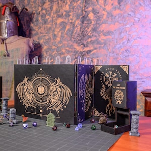 Könnte beinhalten: Ein schwarzes Tischspielset mit Drachen- und geometrischem Design. Das Set enthält einen Würfelturm, einen Sichtschutz und verschiedene Würfel. Der Sichtschutz hat ein Drachen- und Runen-Design. Der Würfelturm hat den Text "Let the dice decide".